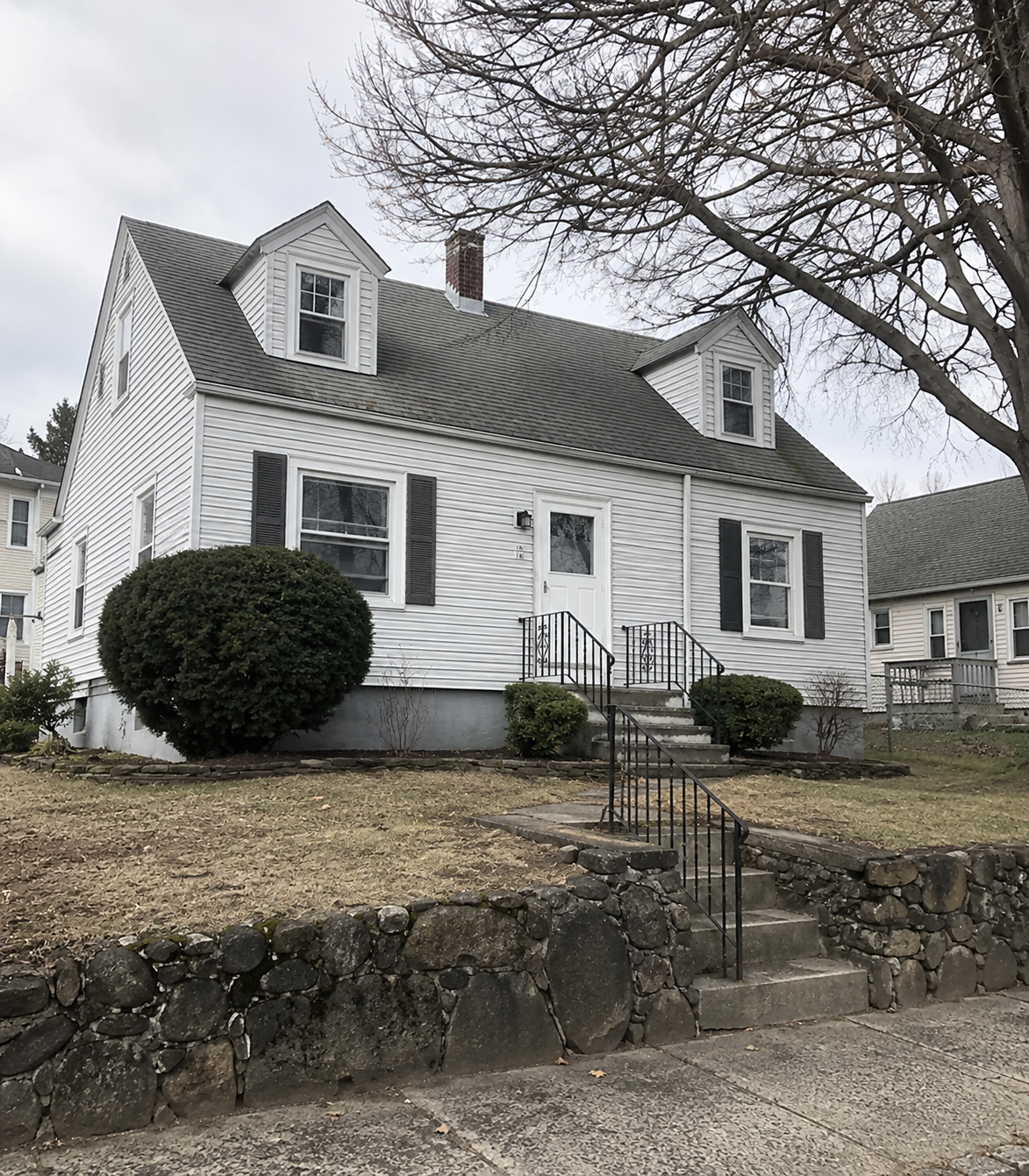 A modest 1960s Cape Cod-style house in a Worcester, Massachusetts neighborhood, vinyl siding and original single-pane windows